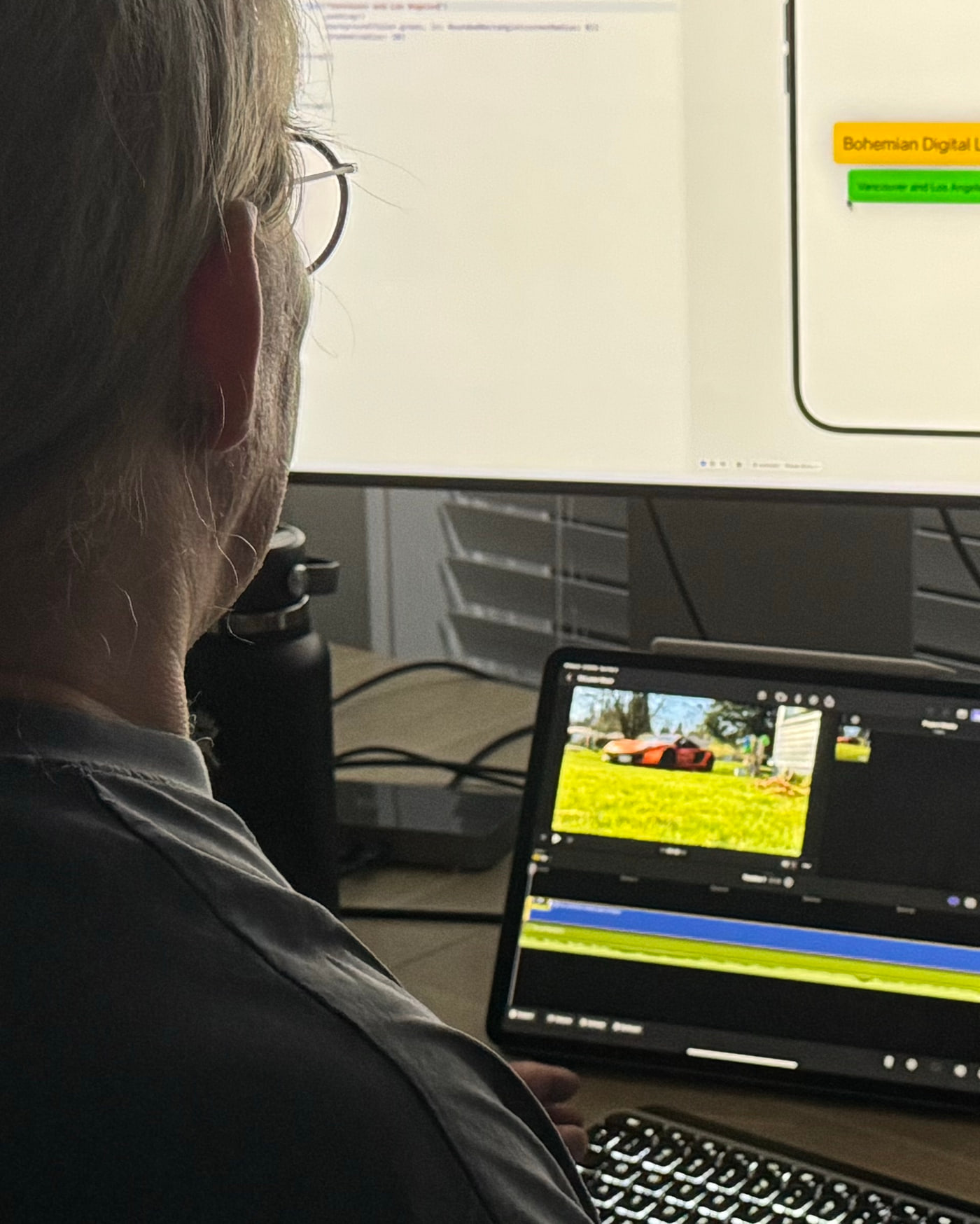 Over-the-shoulder view of a Bohemian Digital workstation: an app prototype on the main display, a mind map on a second screen and a video edit in progress on an iPad.